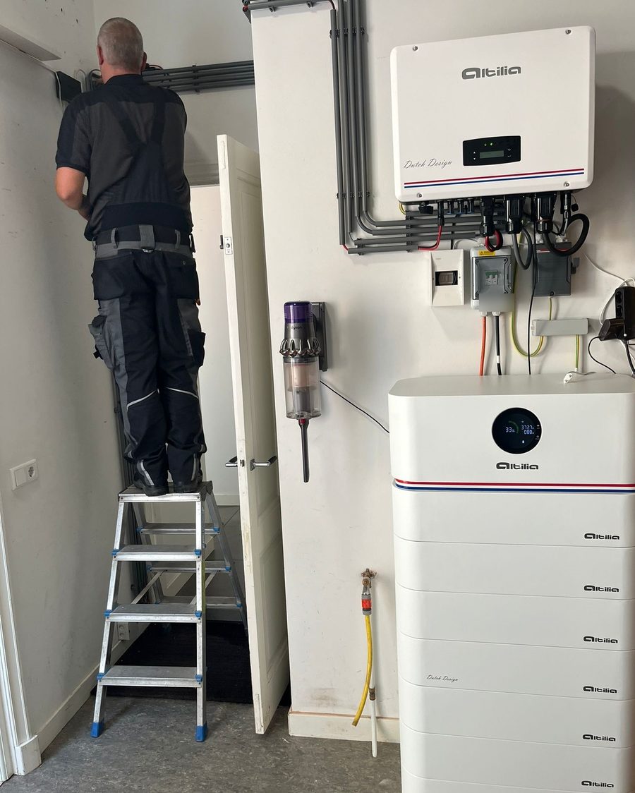 Altilia stapelbatterij met omvormer in een woning, met een monteur op een trapje aan het werk