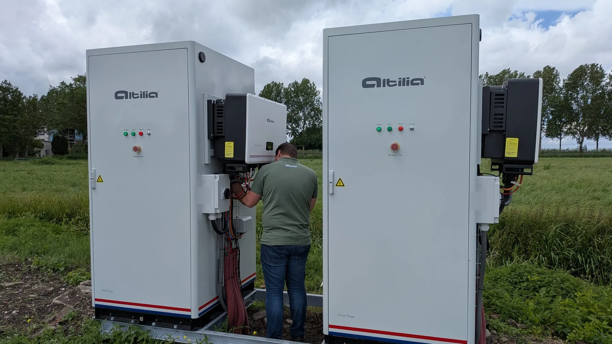 Twee energieopslagsystemen van Altilia in de polder, een monteur sluit de omvormer aan